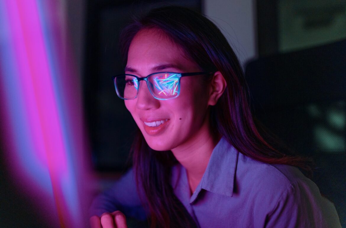 How screen time affects your eyes: Portrait of a woman with blue light glasses working on a computer at night