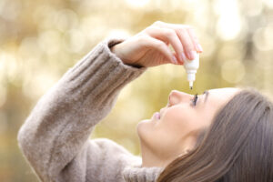 how to get rid of winter allergies: Woman with dry eyes applying artificial tear in winter