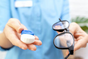 optometrist holding eyeglasses in one hand and a case for contacts in the other