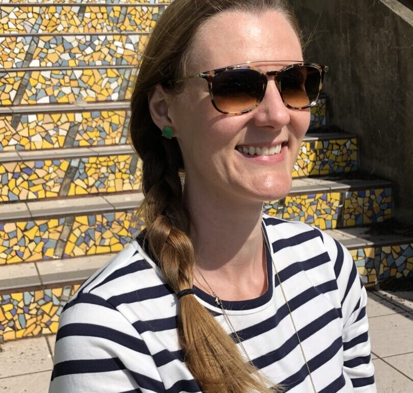 woman smiling outside in a striped shirt with polarized sunglasses for UV eye protection