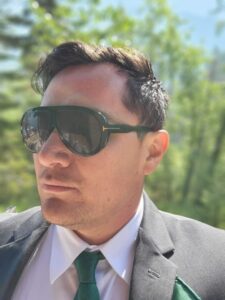 man in a suit standing outside in the sun wearing large polarize sunglasses for eye protection