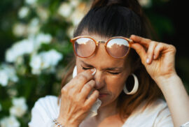 Summer time. sad woman in white shirt with handkerchief and eyeglasses dealing with summer eye allergies near a flowering tree.