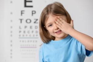 Little girl getting a pediatric eye exam; covering her eye against vision test chart
