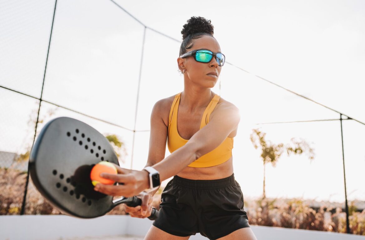 Woman playing beach tennis serving and wearing prescription sports goggles to prevent eye injury