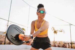Woman playing beach tennis serving and wearing prescription sports goggles to prevent eye injury